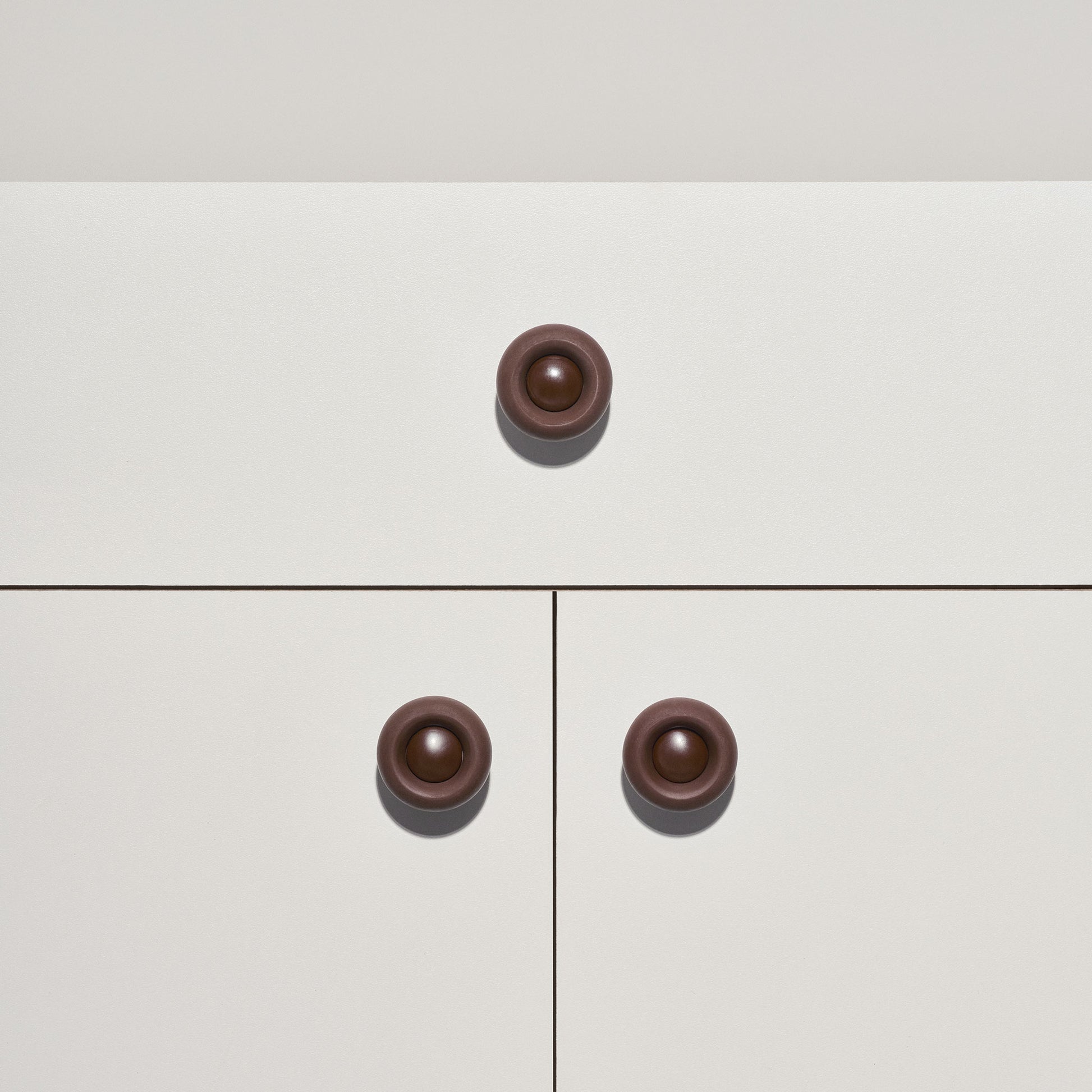 White cabinet with chocolate brown  colored cabinet knobs on a white background