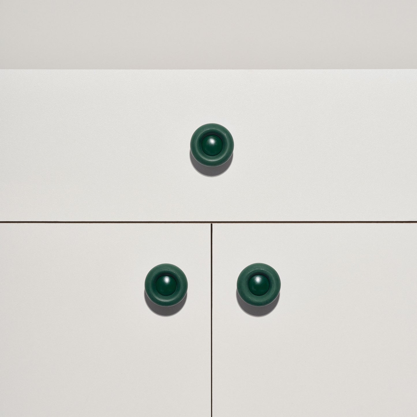 White cabinet with dark green colored cabinet knobs on a white background