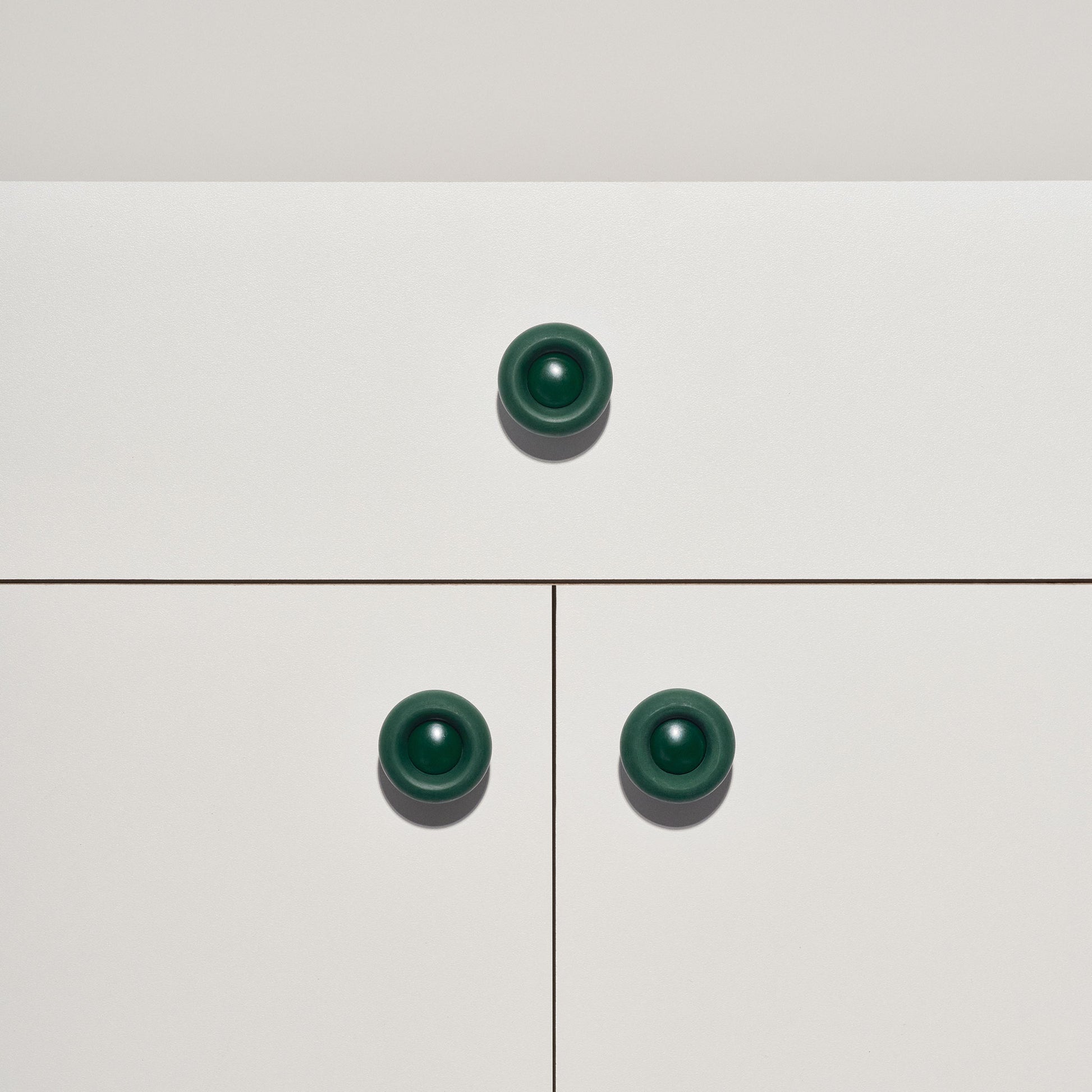 White cabinet with dark green colored cabinet knobs on a white background