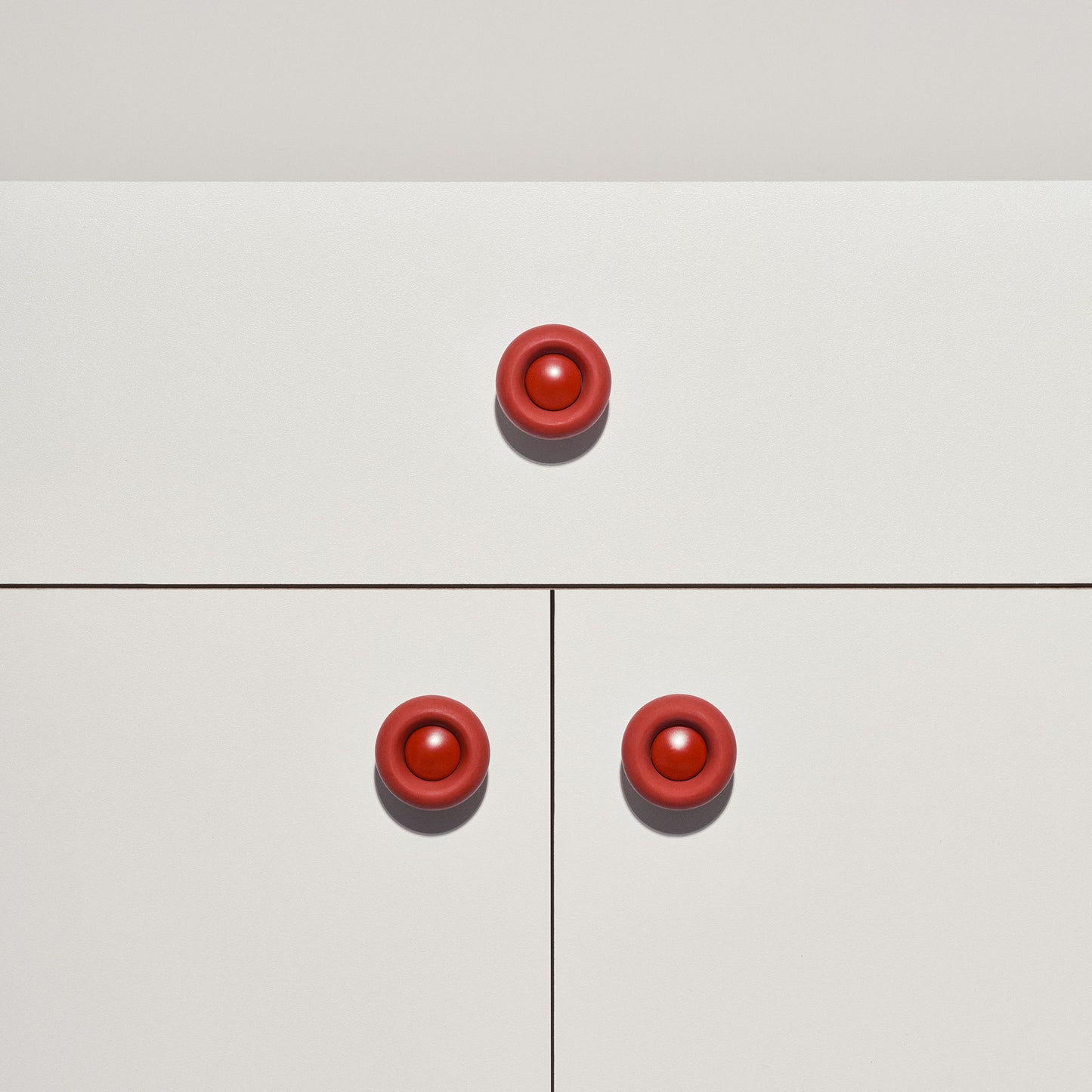 White cabinet with red colored cabinet knobs on a white background