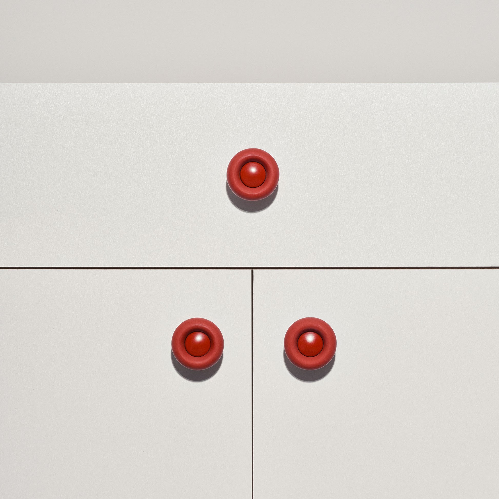 White cabinet with red colored cabinet knobs on a white background