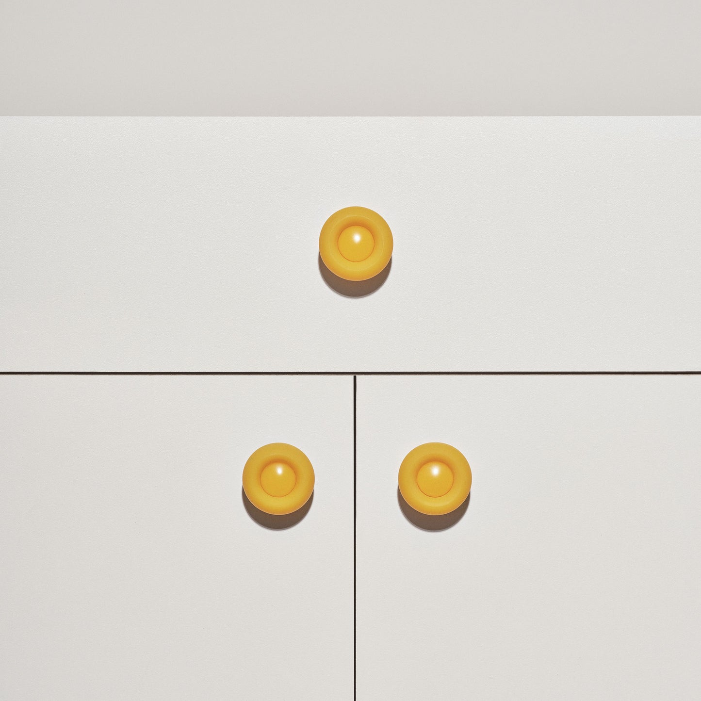 White cabinet with yellow colored cabinet knobs on a white background