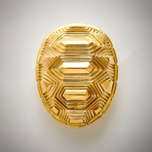 An oval-shaped decorative cabinet pull featuring a textured polished natural brass geometric pattern, on a neutral light gray background.