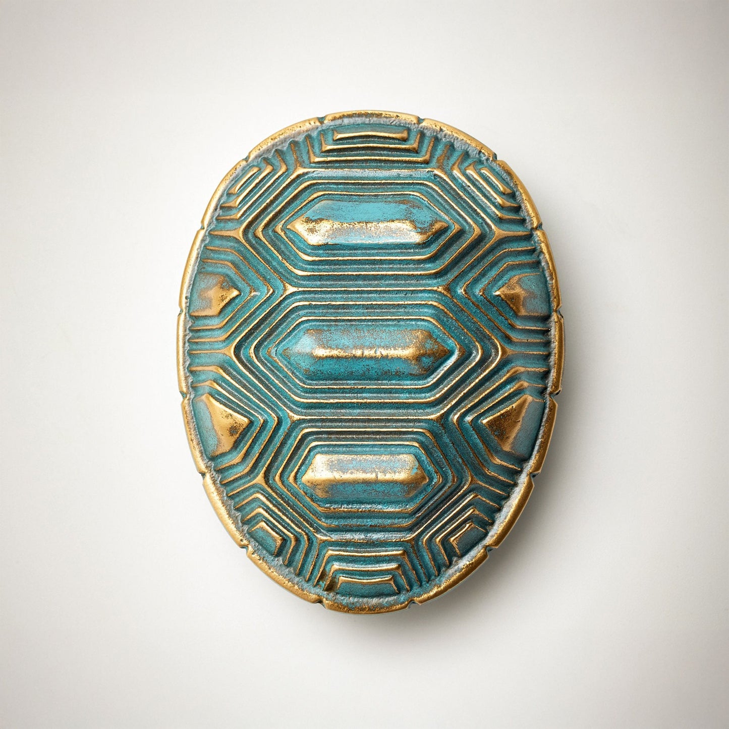 An oval-shaped decorative cabinet pull featuring a textured turquoise and gold geometric pattern, on a neutral light gray background.