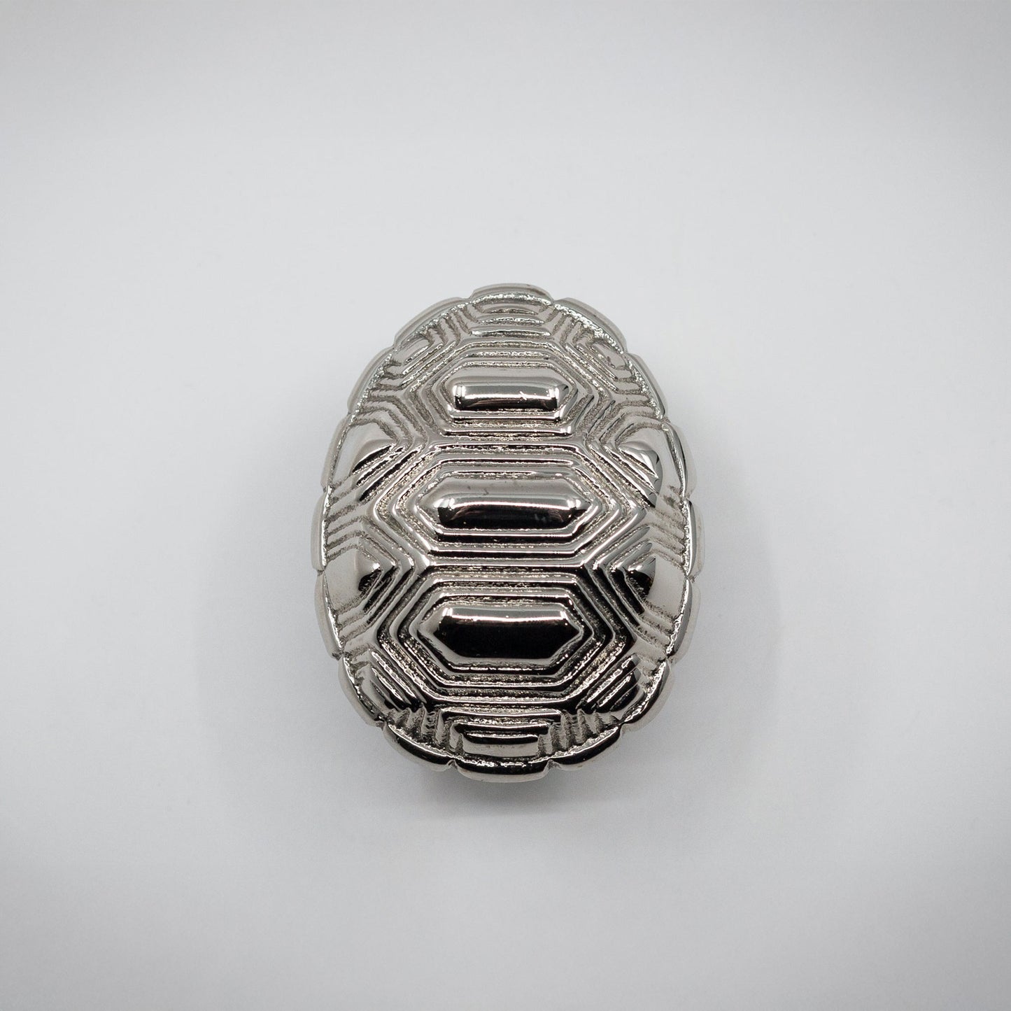 A small silver-toned polished nickel tortoise shell cabinet hardware pull on an off-white background.