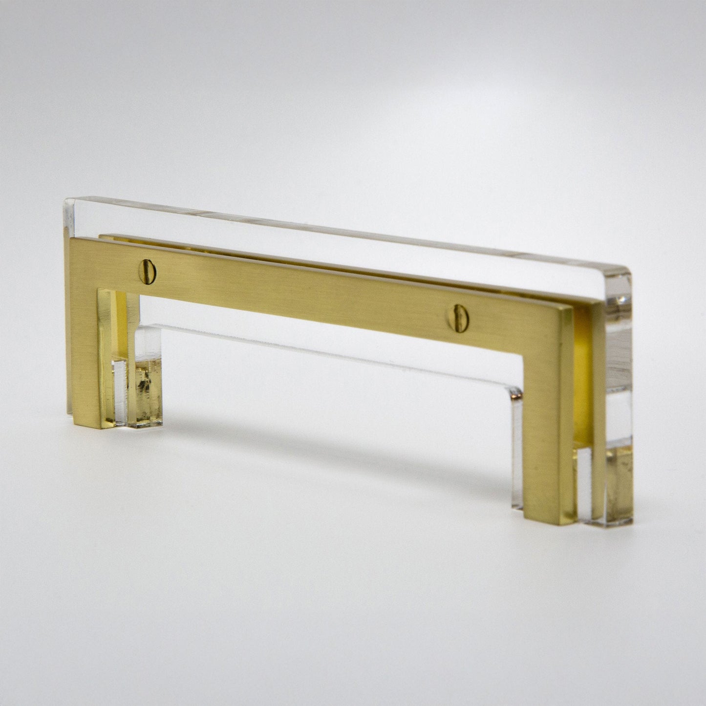 A modern rectangular cabinet pull handle made of brushed gold metal and clear acrylic, shown on a clean white background.