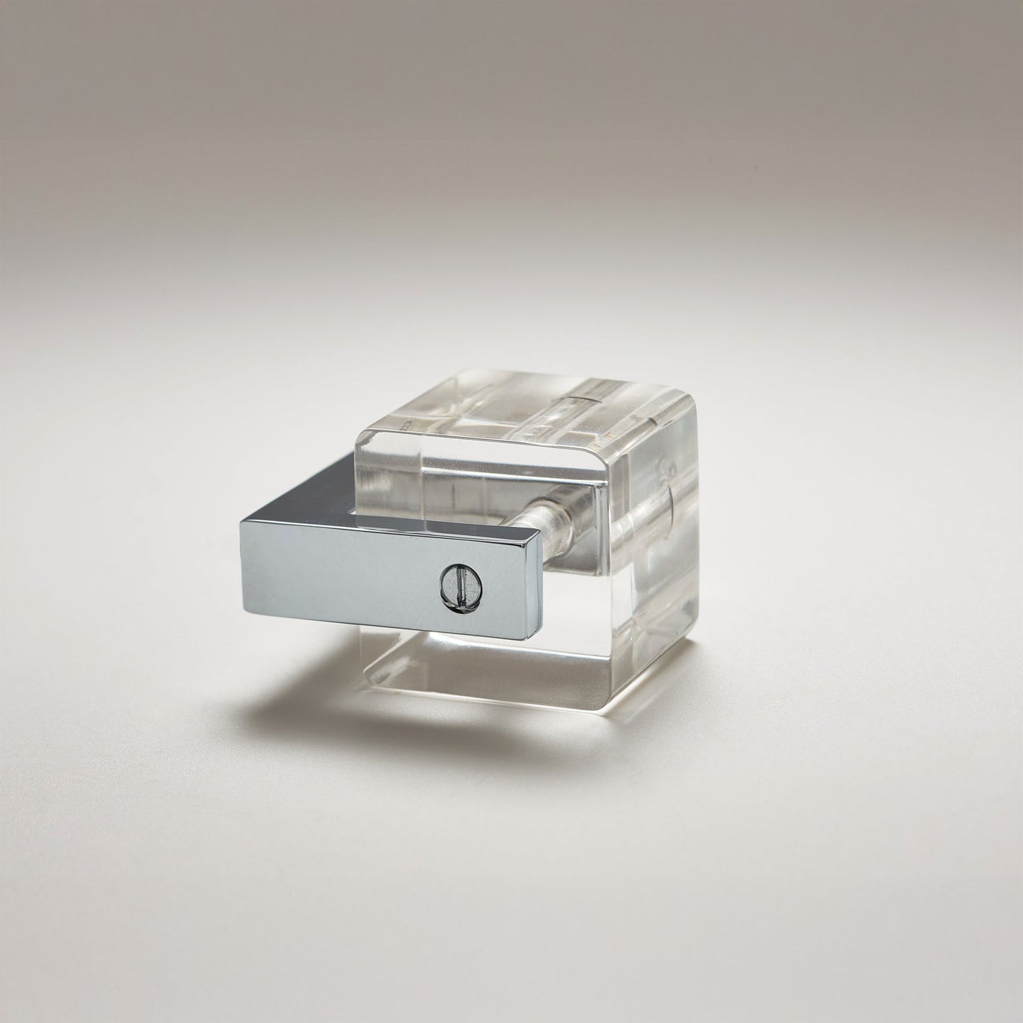 A modern acrylic cabinet knob with a clear, geometric cube design and a polished silver metal cap, set against a neutral light gray background.