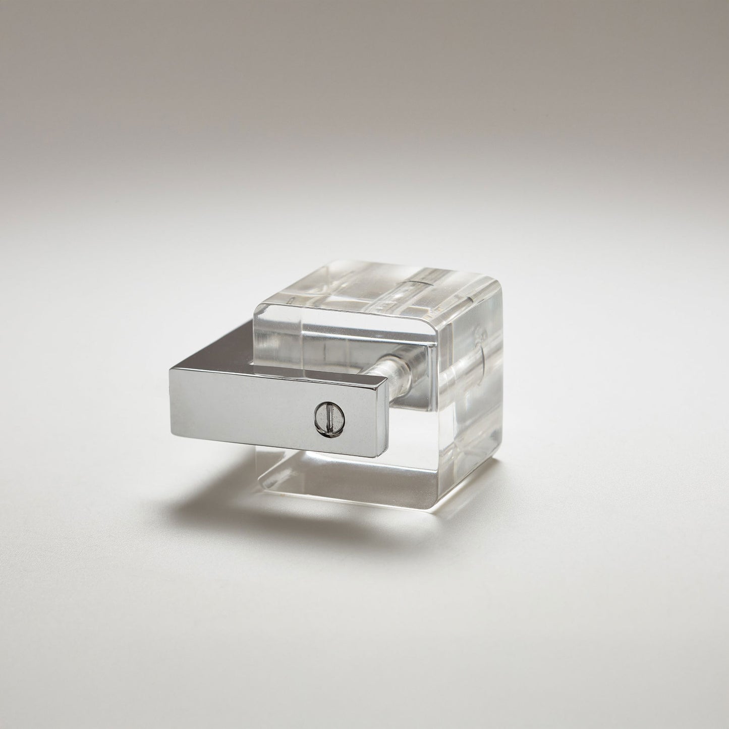 A clear acrylic cabinet knob with a polished silver metal collar and a single screw detail, set against a neutral light gray background.