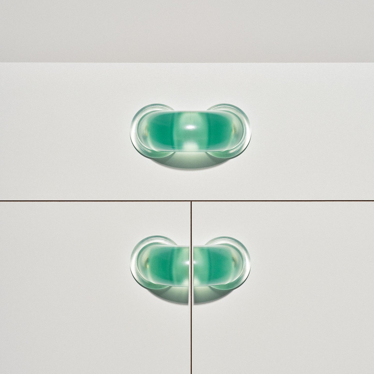 White cabinet with translucent green colored macaroni-shaped handles on a white background