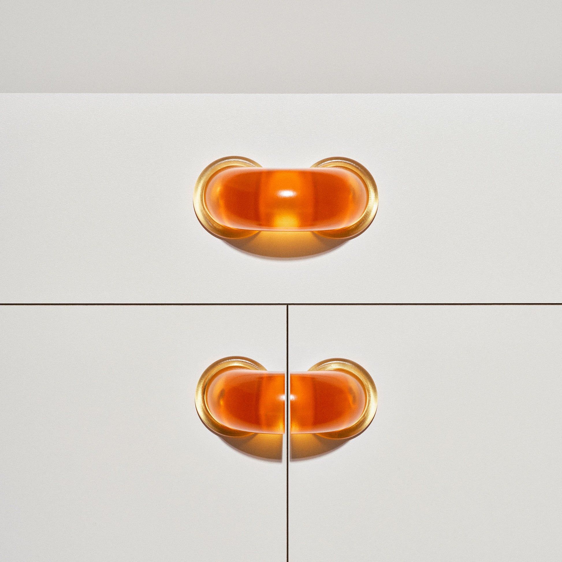 White cabinet with translucent orange colored macaroni-shaped handles on a white background