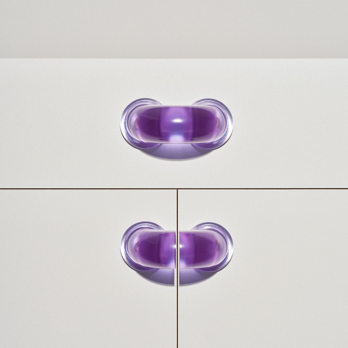White cabinet with translucent purple colored macaroni-shaped handles on a white background