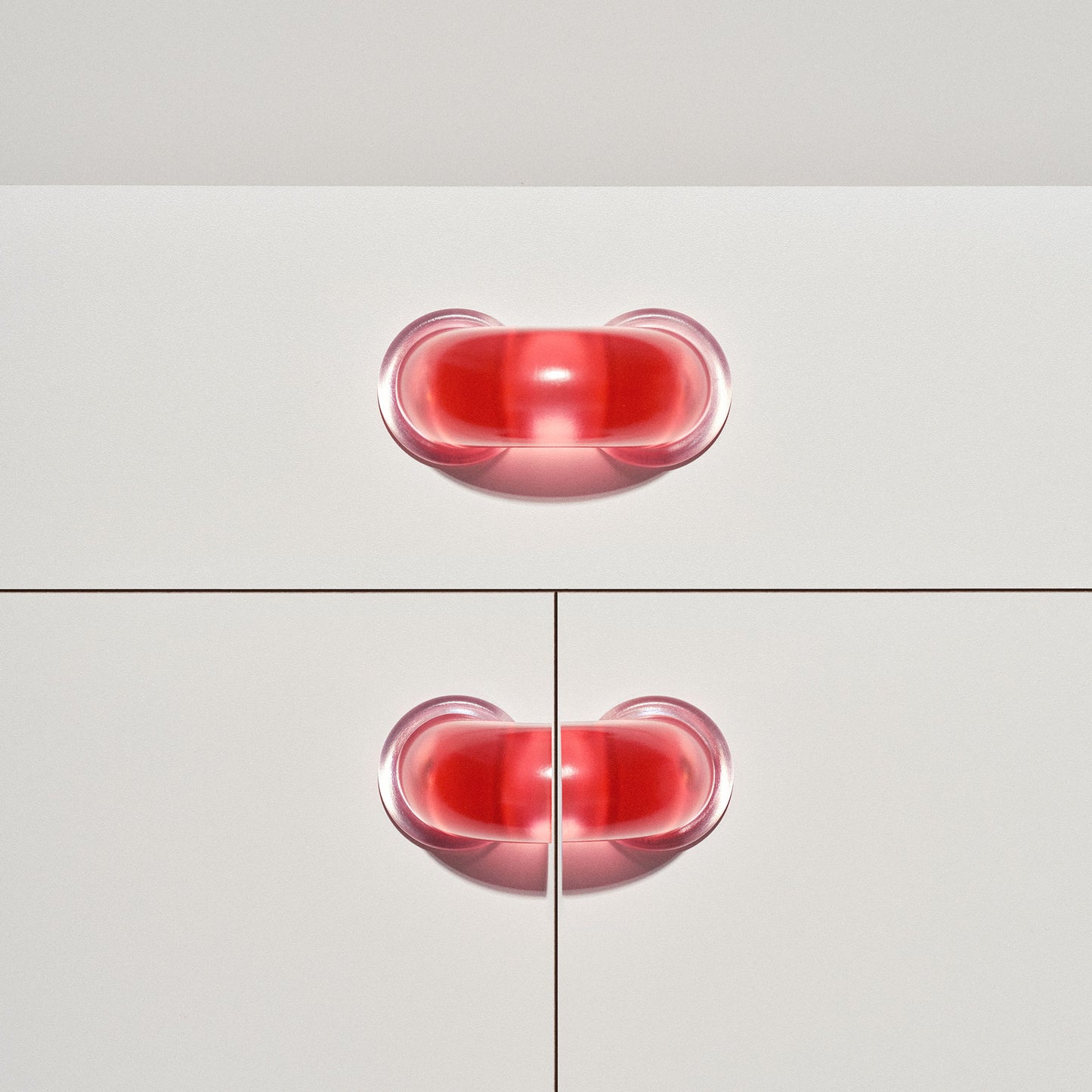 White cabinet with translucent red colored macaroni-shaped handles on a white background