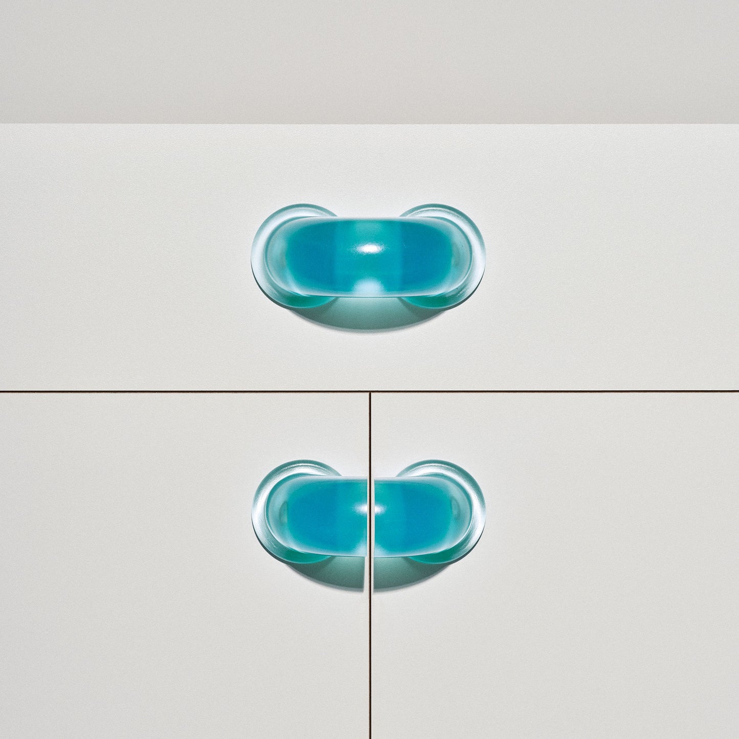 White cabinet with translucent blue colored macaroni-shaped handles on a white background