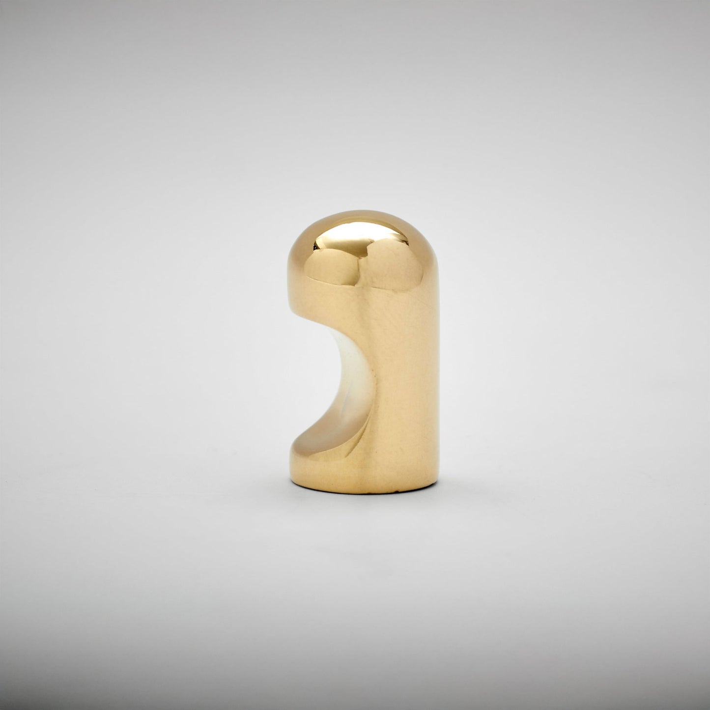 A small metallic cabinet knob with a rounded top and a curved cutout on the side, photographed on a clean light gray studio background.