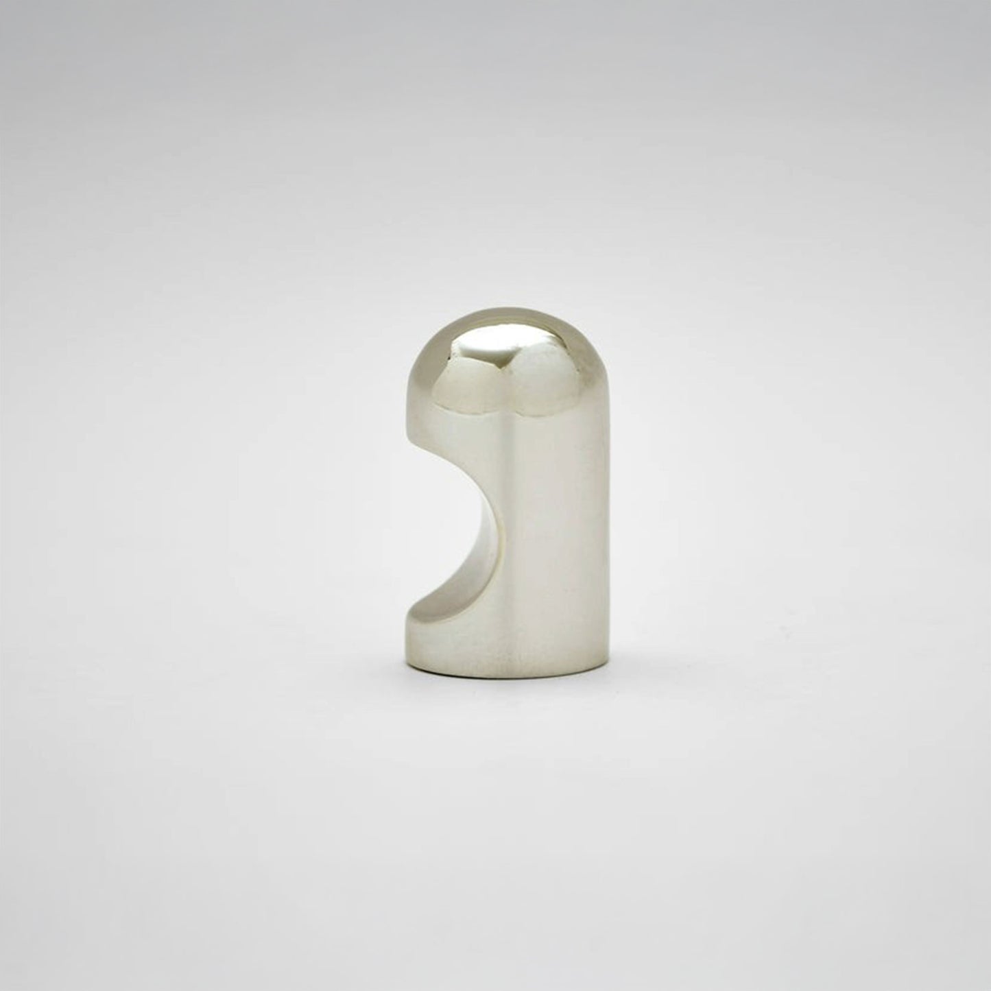 A small metallic cabinet knob with a rounded top and a curved cutout on the side, photographed on a clean light gray studio background.
