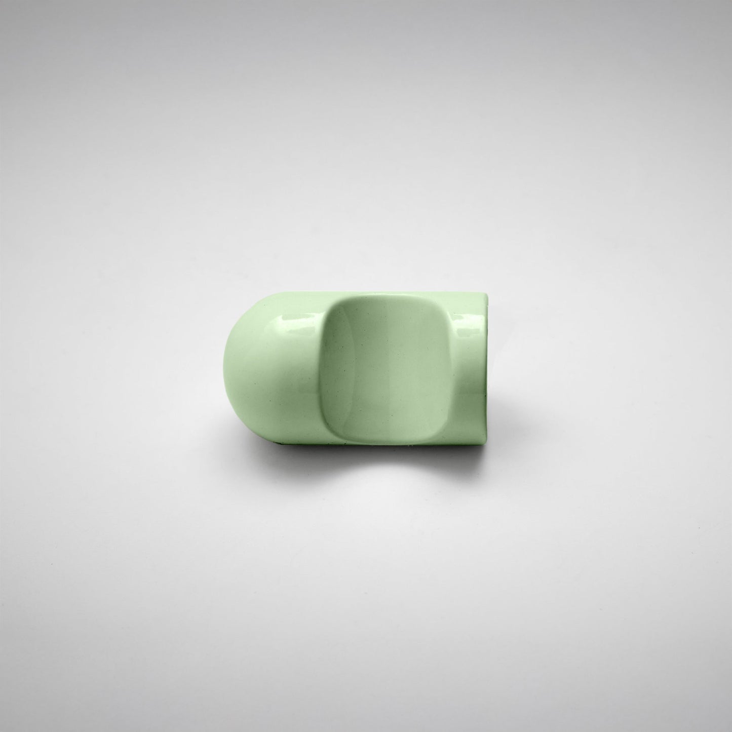 A glossy light green cabinet pull with a rounded, modern dome-like shape, photographed on a neutral light gray background.
