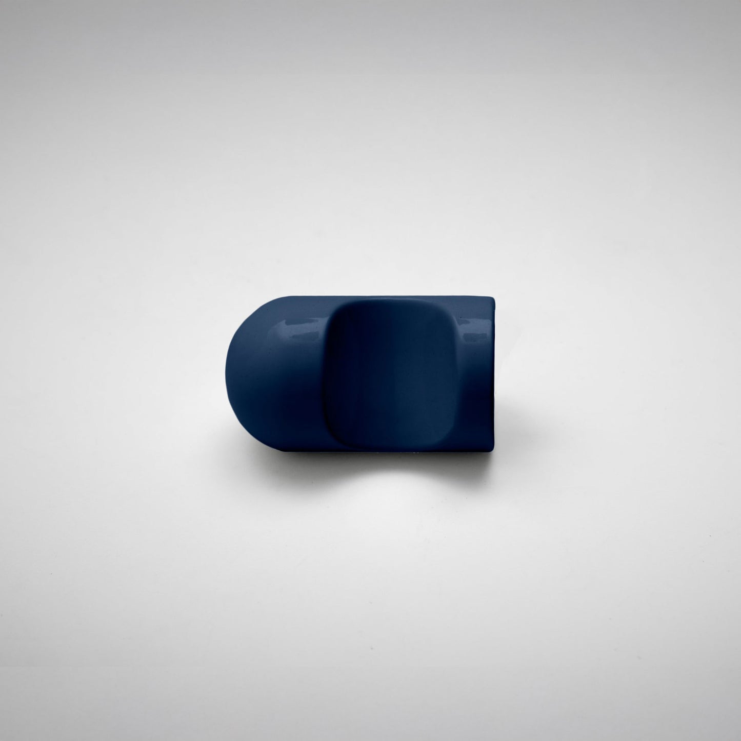 A glossy navy blue cabinet pull with a rounded, modern dome-like shape, photographed on a neutral light gray background.