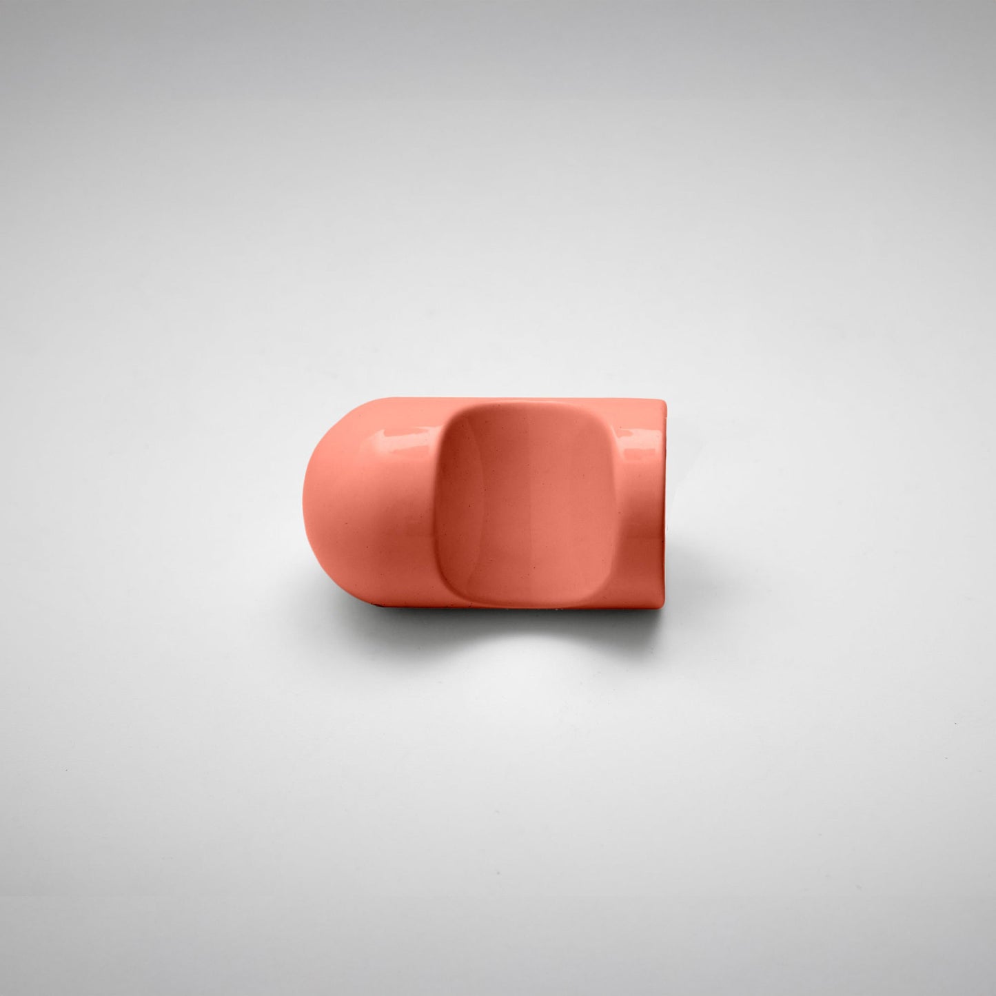 A glossy coral pink cabinet knob with a rounded dome-shaped top and a central recessed opening, shown on a neutral light gray background.