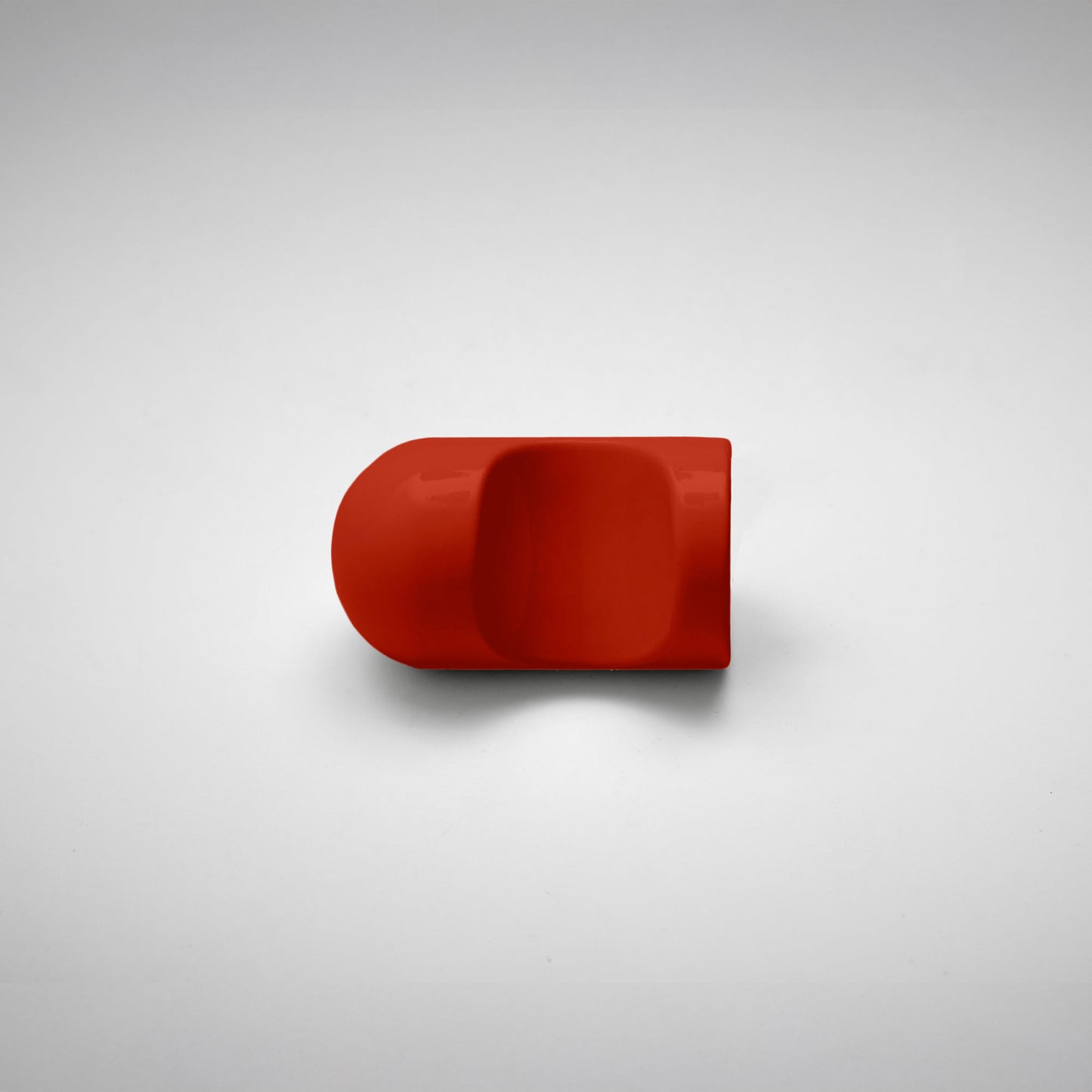 A glossy red cabinet pull with a rounded, modern dome-like shape, photographed on a neutral light gray background.