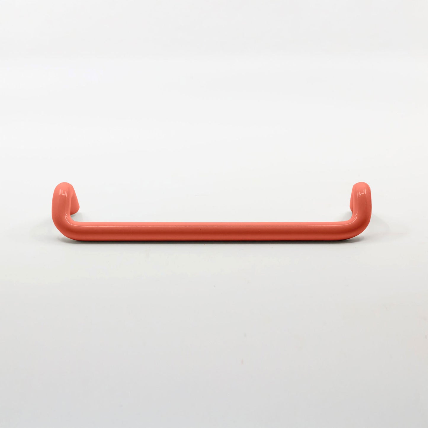 A single curved cabinet pull handle in a matte coral-red finish, photographed against a seamless white background.