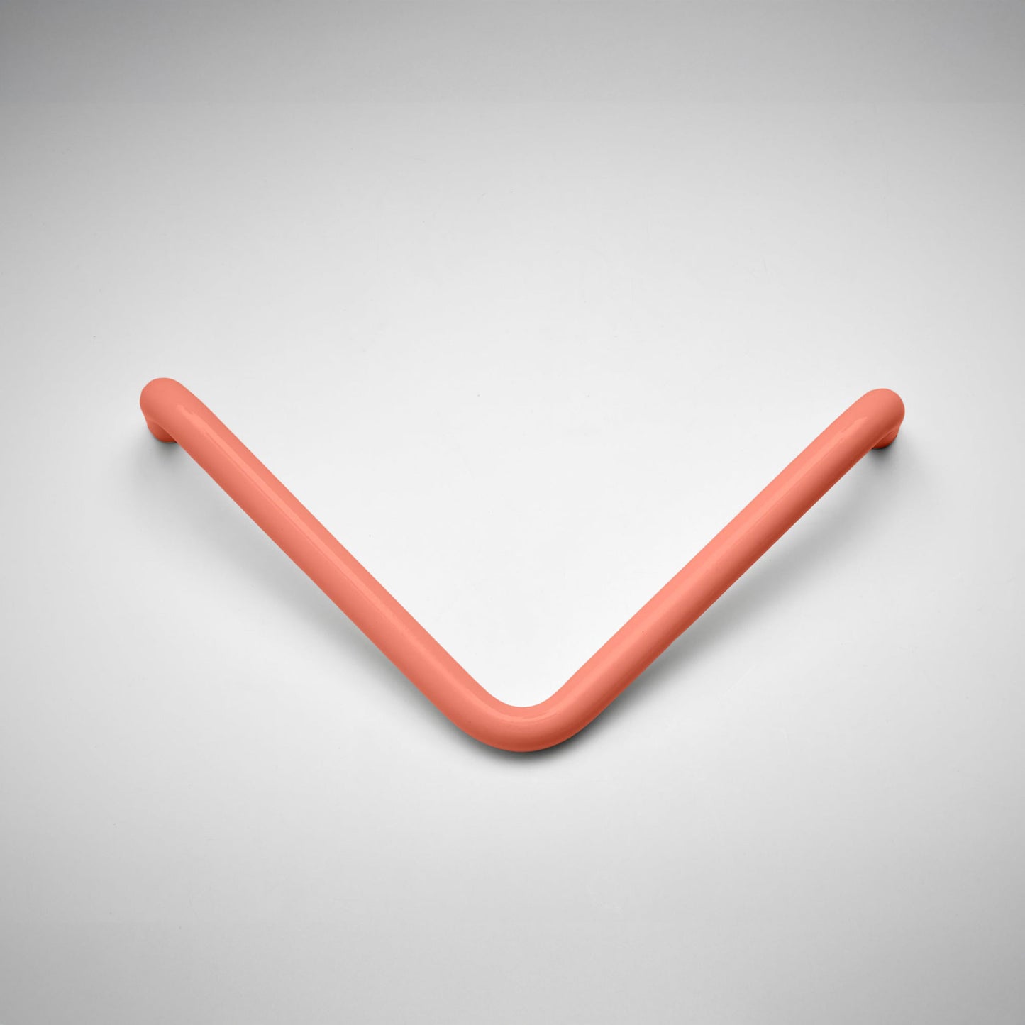 A modern, curved V-shaped metal cabinet pull in a matte coral pink finish, photographed on a clean light gray background.