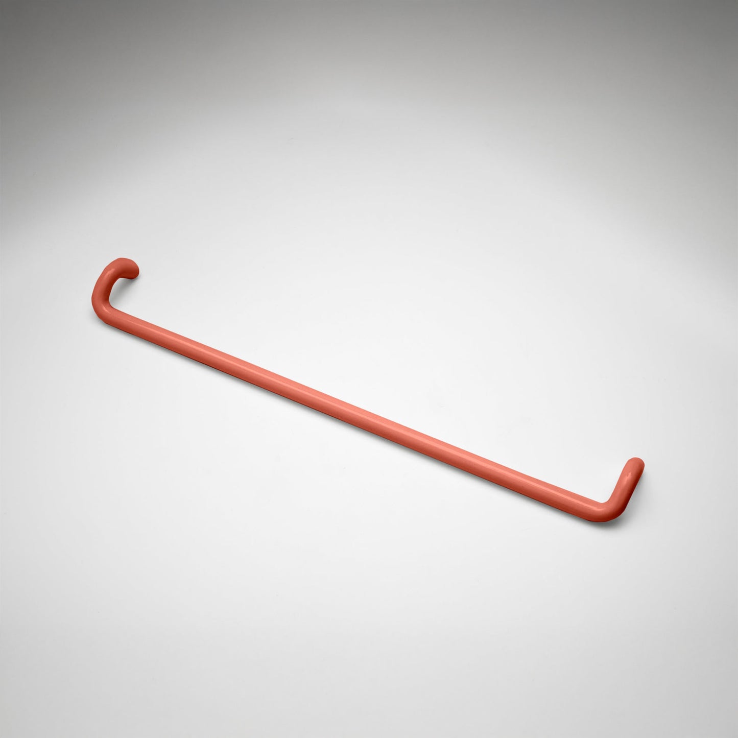 A minimalist salmon colored metal cabinet pull with a curved, modern design, shown on a clean light gray background.