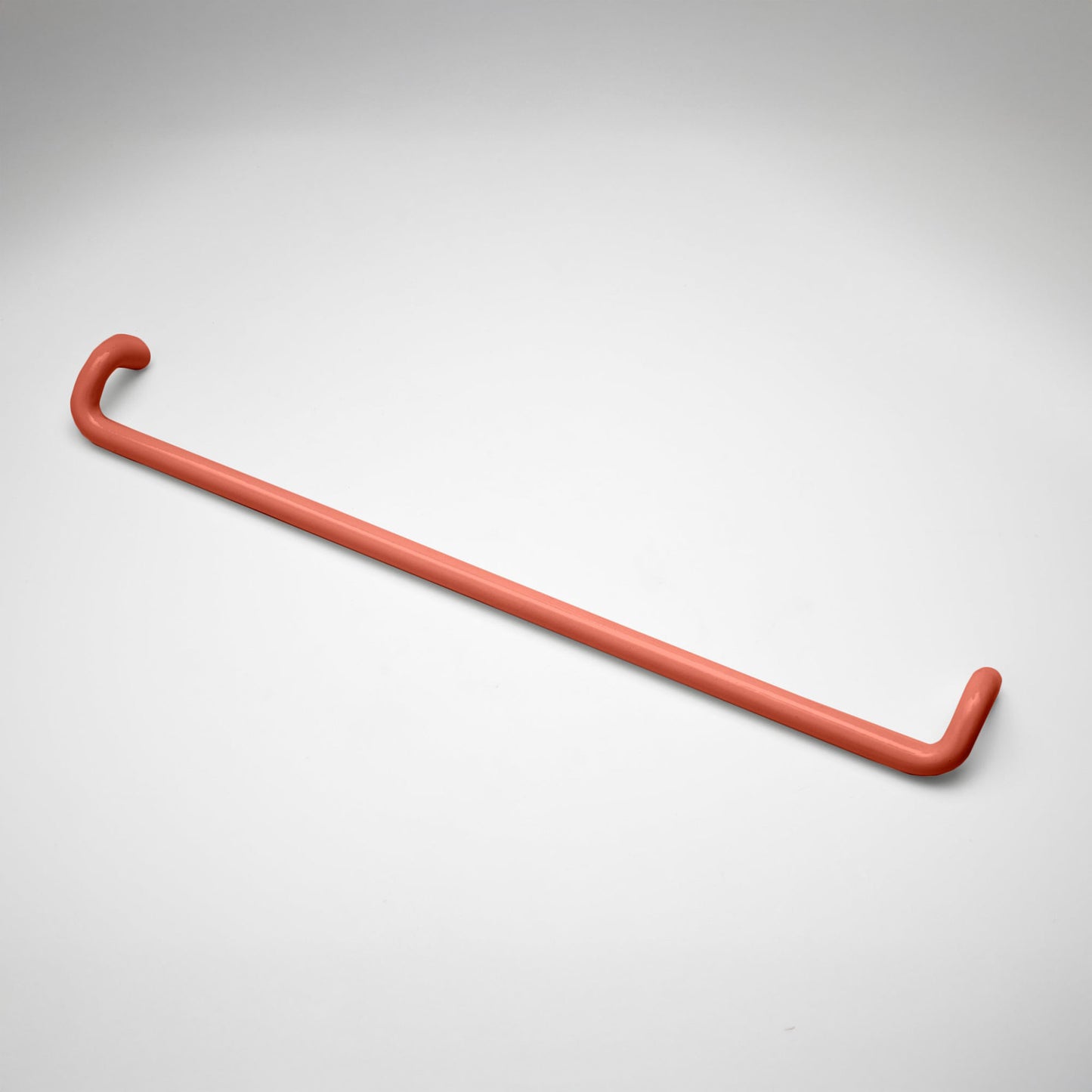 A minimalist coral metal cabinet pull with a curved, modern design, shown on a clean light gray background.