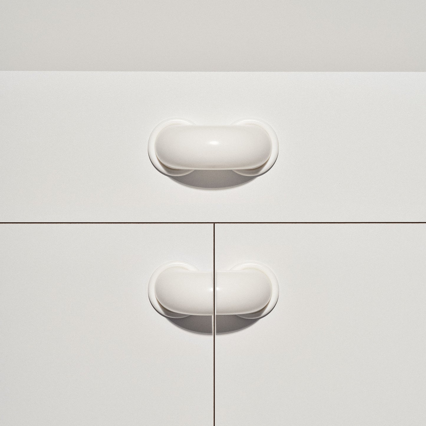White cabinet with signal white colored  macaroni-shaped handles on a white background