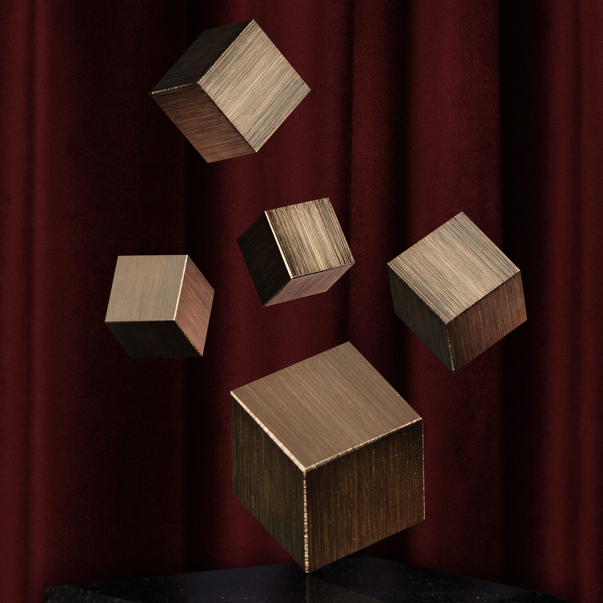 Three gold cube-shaped cabinet knobs falling in front of red drapery